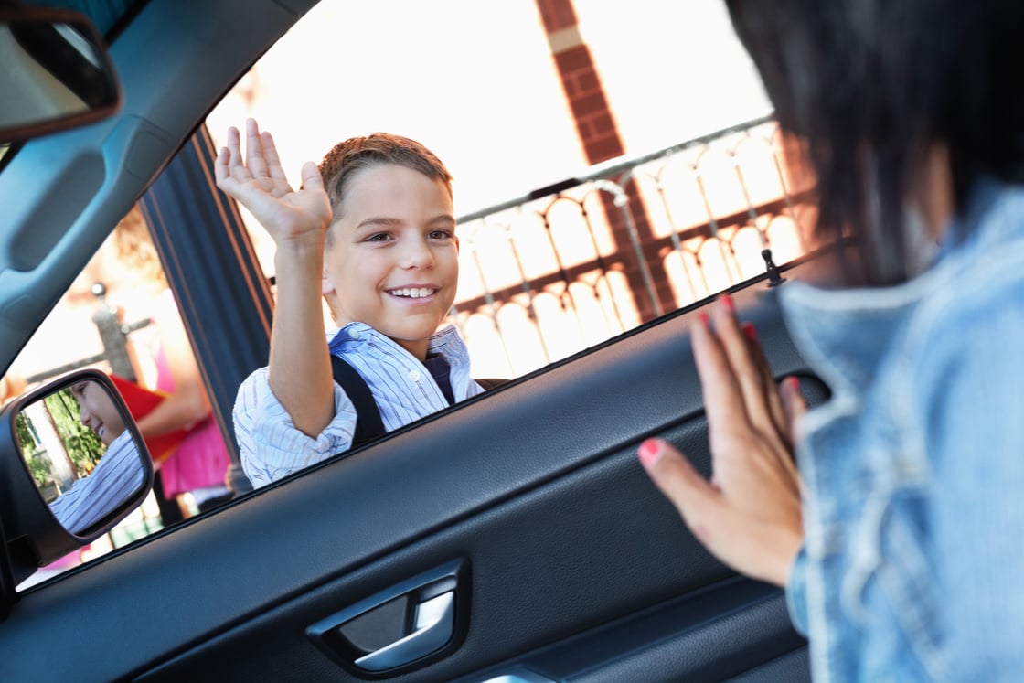 Mother waving to son as he's dropped off at school